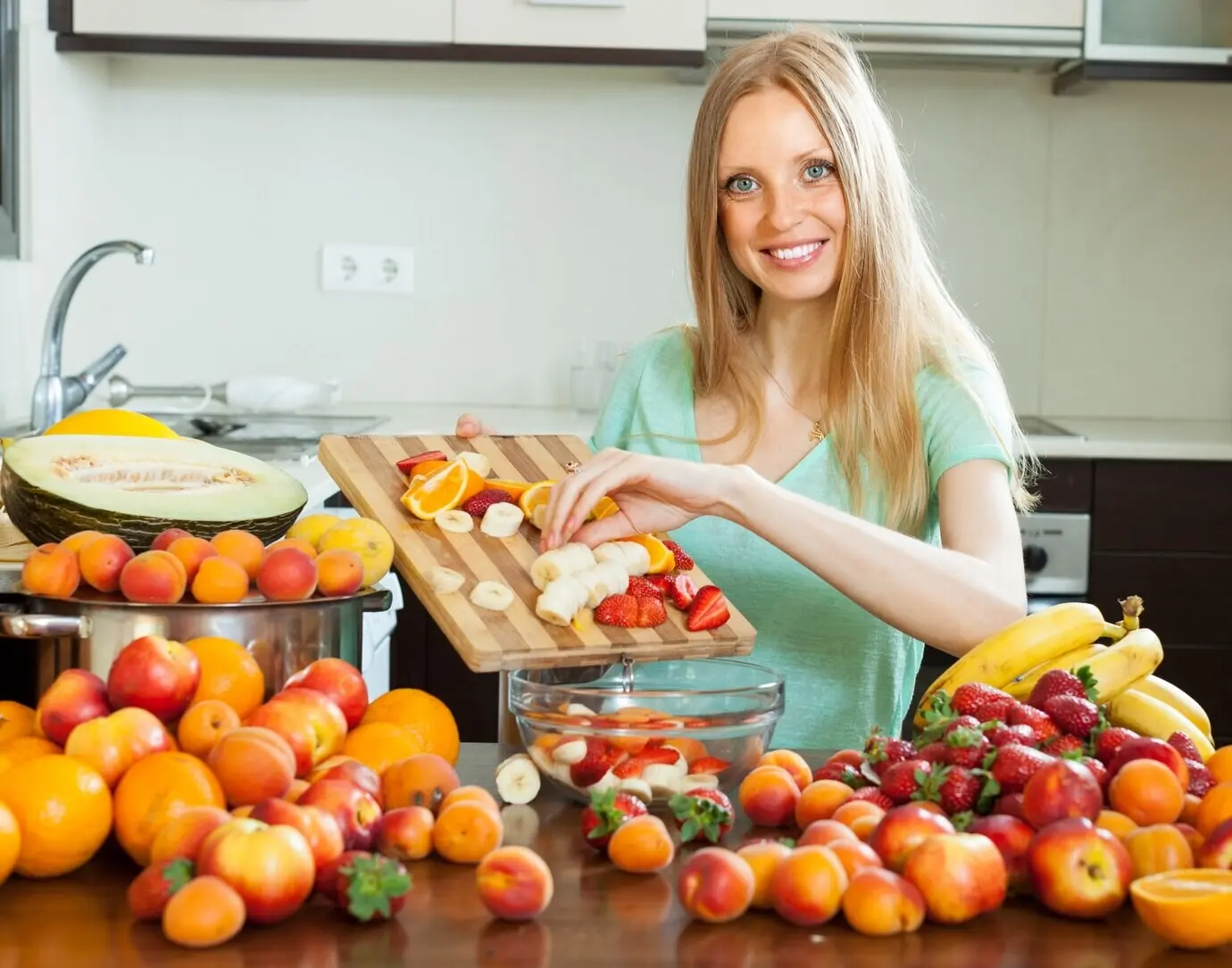 Fröhliche blonde Frau beim Kochen mit reifen Früchten.